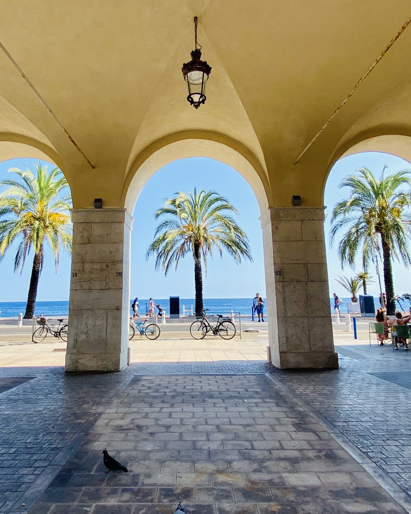 View of the sea and palm trees through the stone arcades of the Promenade des Anglais in Nice