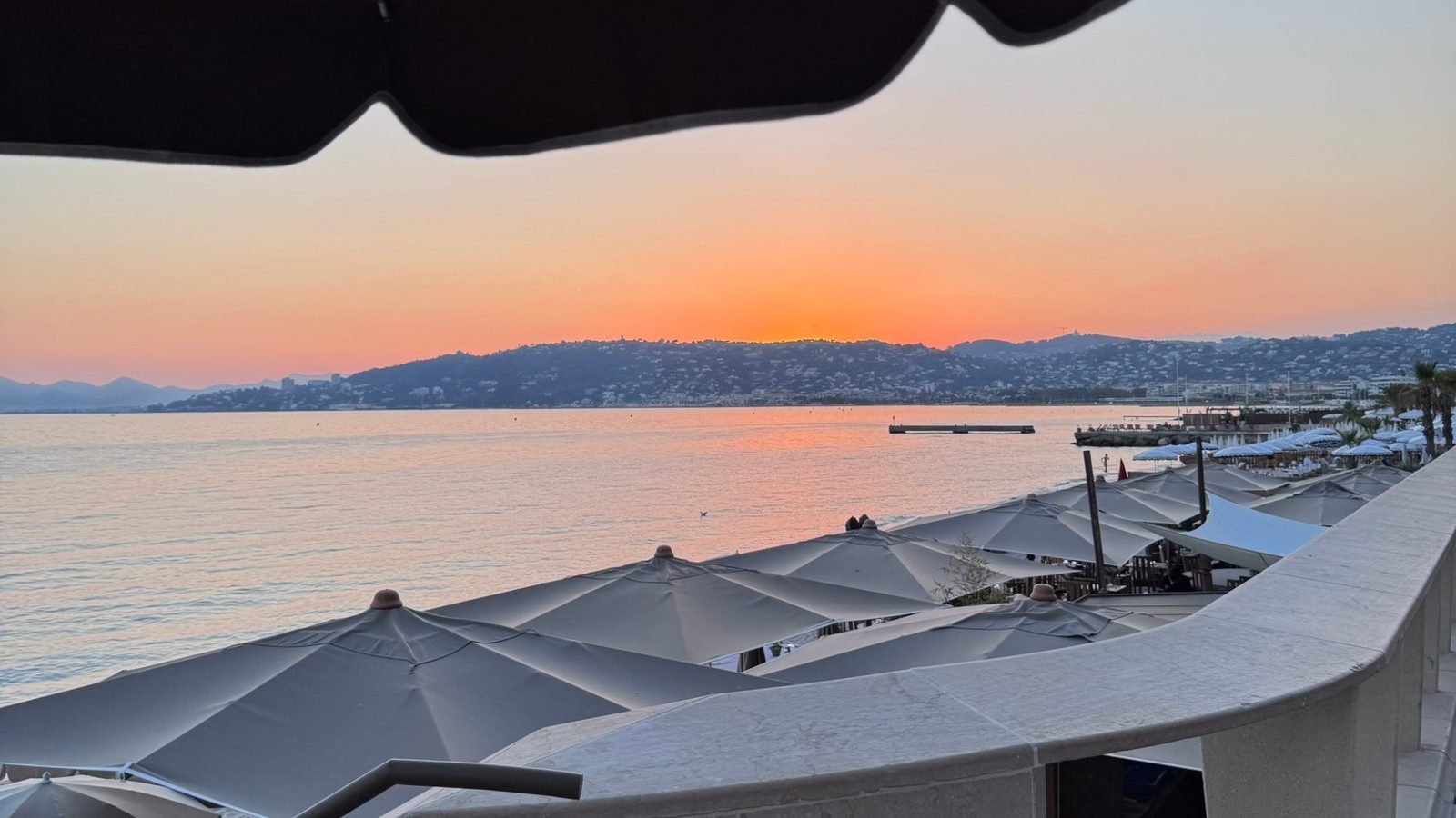 The coast in low golden October light (Baie des Anges or Cap d'Antibes), a few people, calm sea.