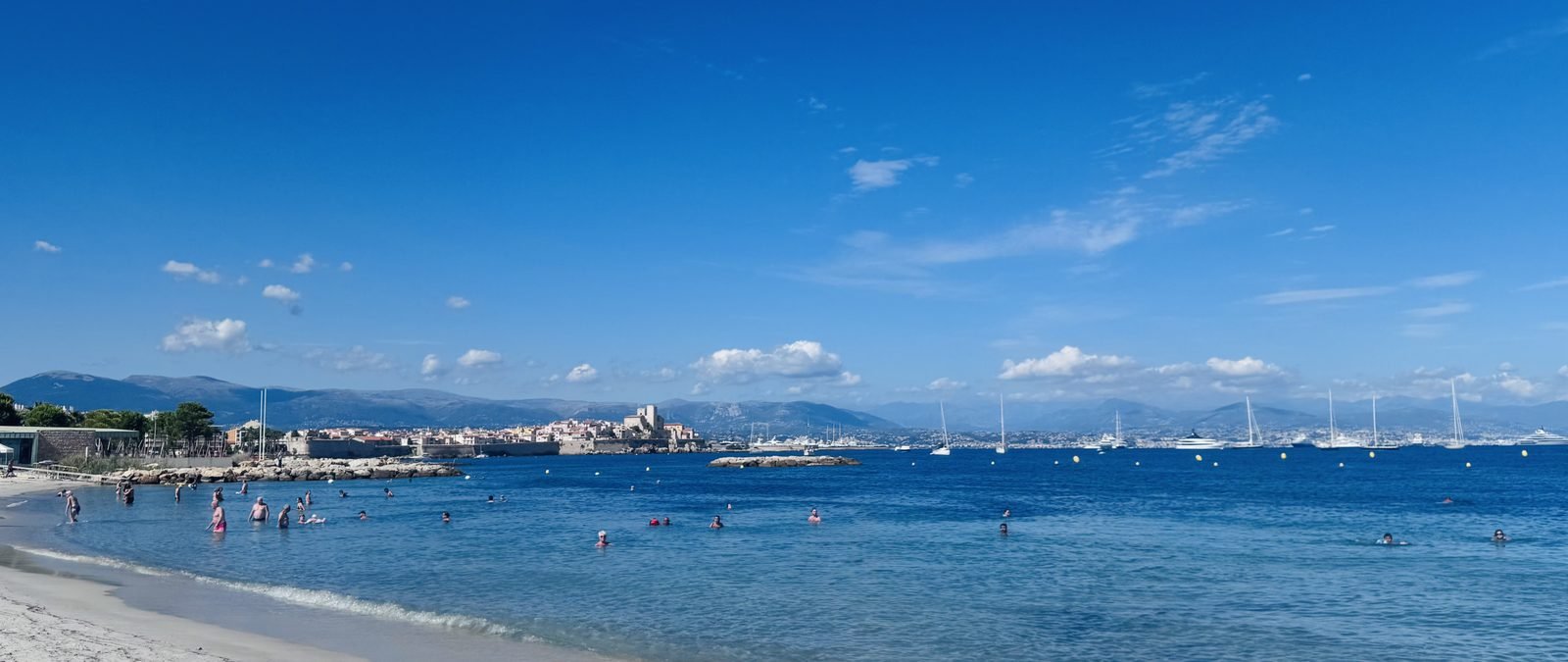 Plage de la Salis in Antibes, ramparts across the bay, a lone swimmer, autumn light.