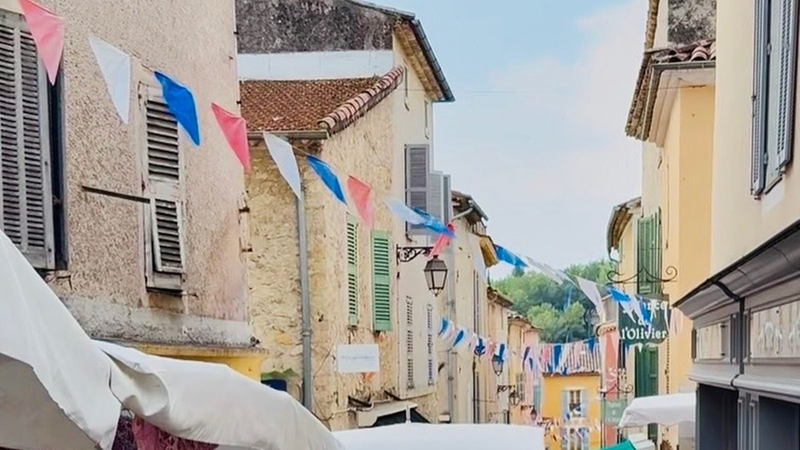 Rue Grande in Valbonne dressed with bunting for market day, awnings over the stalls and shoppers browsing.